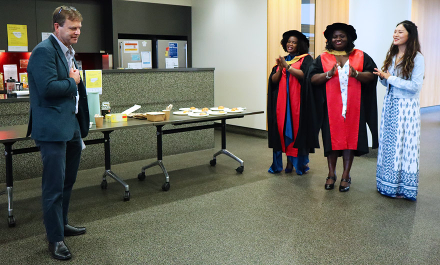 The director of the Kirby Institute, Professor Anthony Kelleher giving a congratulatory speech to three women - two of them are in PhD graduation gowns